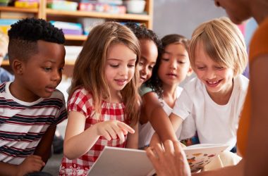 Group Of Elementary School Pupils Sitting On Floor Listening To Female Teacher Read Story