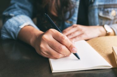 Closeup image of a woman writing on a blank notebook on the table